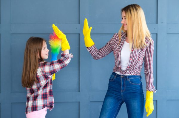 Mother and daughter giving a high five while wearing yellow plastic cleaning gloves as daughter holds a rainbow colored feather duster.