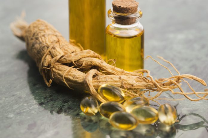 Ginseng root sitting next to two vials of ginseng extract and a handful of gel capsules.