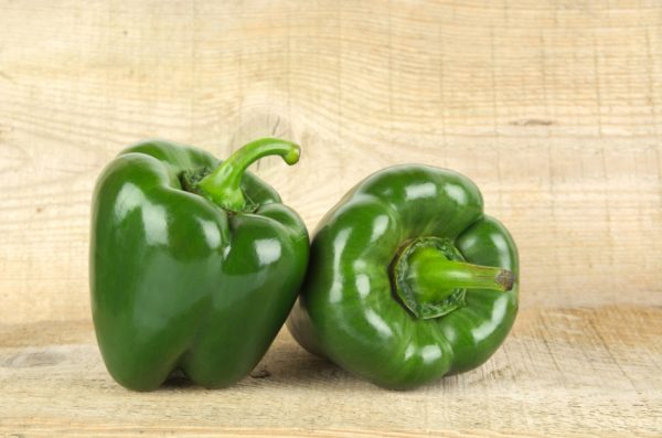 Two green bell peppers sitting on a wooden table.