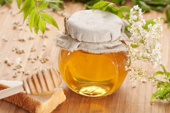 A jar of honey sits on a wooden surface next to a honey dipper.