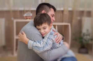 Sad boy hugging his dad indoors.