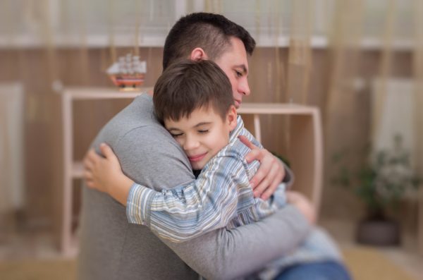 Sad boy hugging his dad indoors.