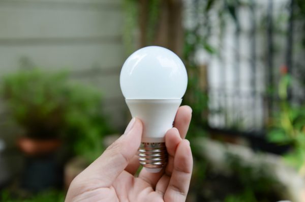 Closeup of a woman's hand holding an LED lightbulb outdoors.