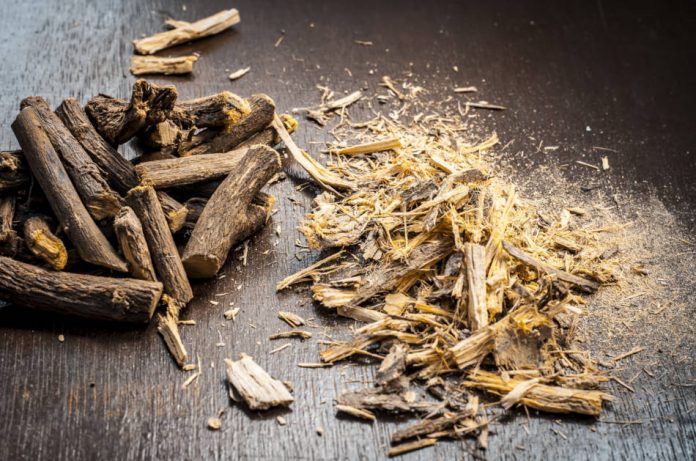Licorice root and licorice root powder sitting on a wooden surface.