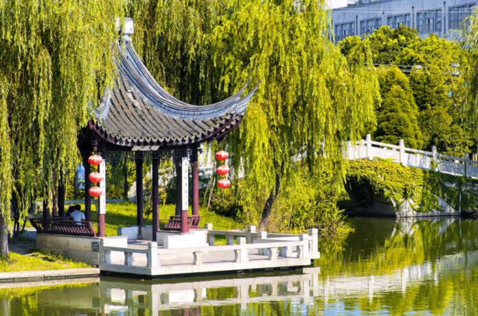 A Chinese gazebo surrounded by weeping willow trees on a small lake within the Luzhi Ancient Town scenic area on a sunny day in Wuzhong China.