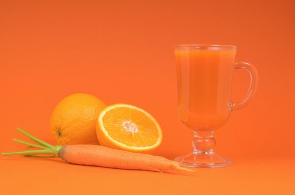 A carrot sits next to an orange and a glass mug full of an orange-carrot smoothie.