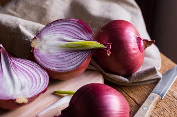 Purple onions sitting on a cutting board beside a knife.