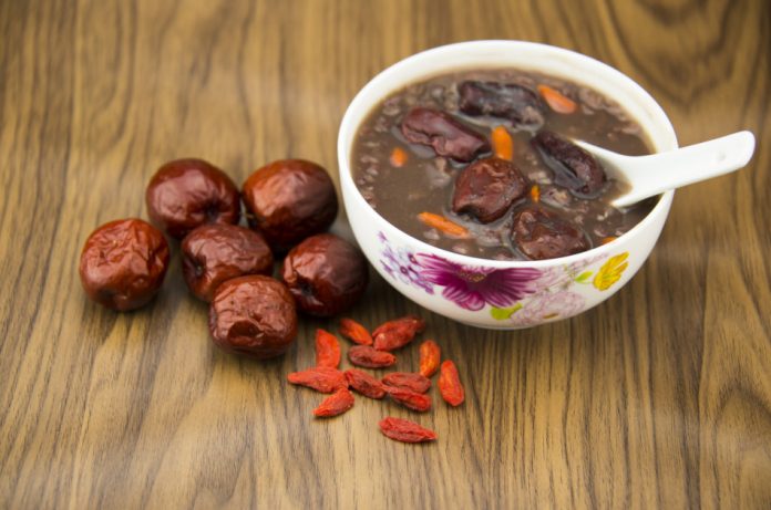Red dates and wolfberry fruit sit on a table with a bowl of porridge.