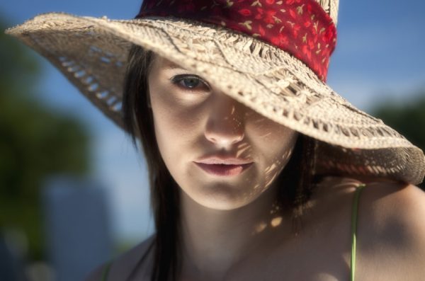 A close up portrait of a twenty something young woman in a sun hat with one eye showing.
