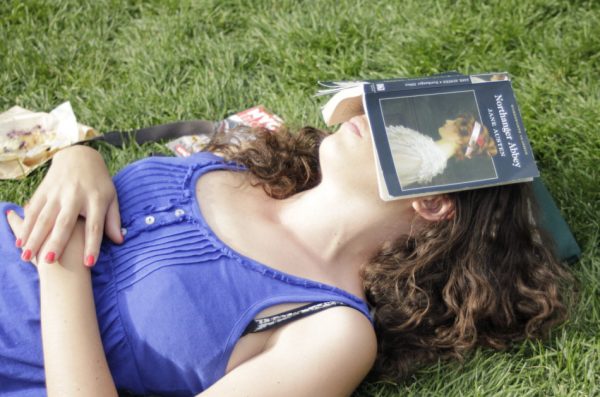 Young woman napping in the grass with a book over her face to block out the sun.