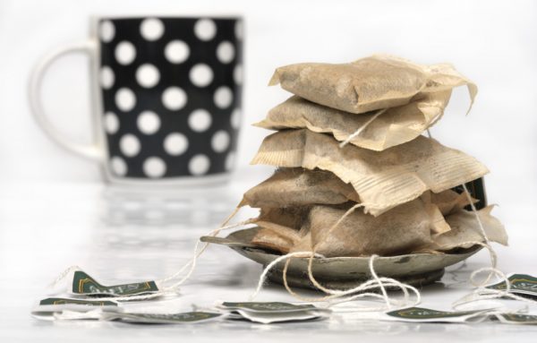 Used tea bags stacked up on a small saucer in front of a black cup with white polka dots.