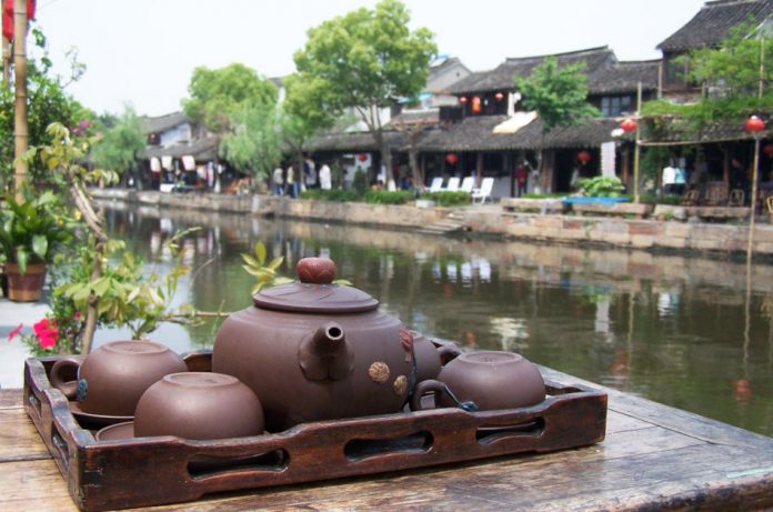 Clay teapot and cups sit on a wooden tray on top of a table next to the scenic waterways in Xitang, one of China's watertowns.
