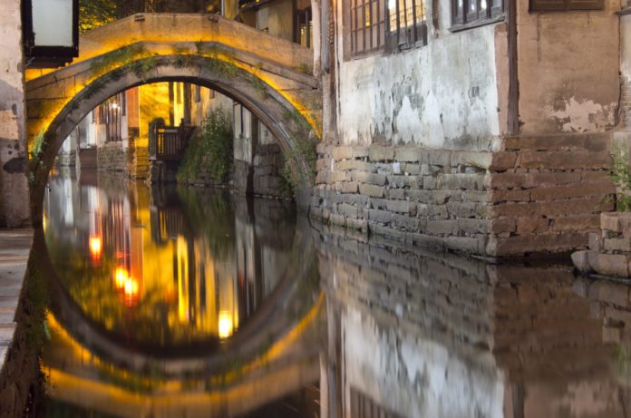 One of the many historical bridges in the water-town of Zhouzhuang, China lit up at night and reflecting in crystal clear water.