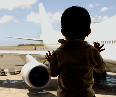 Child kidnapping is rampant all over the world. Shadowed silhouette of the back of a child looking out the window at a plane.