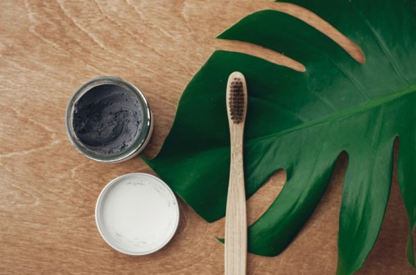 Natural toothpaste activated charcoal and bamboo toothbrush on wooden background with green monstera leaf.