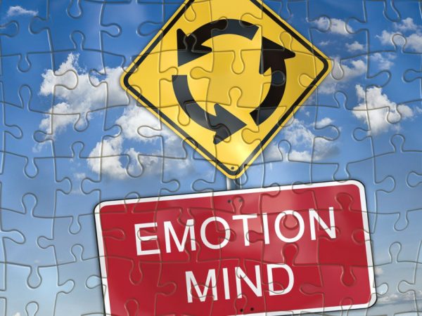 Roadsign showing an upcoming roundabout above a red sign with the words "emotion" and "mind" in white on top of a blue sky background cut into the shape of jigsaw puzzle pieces to illustrate difficulty in making decisions.