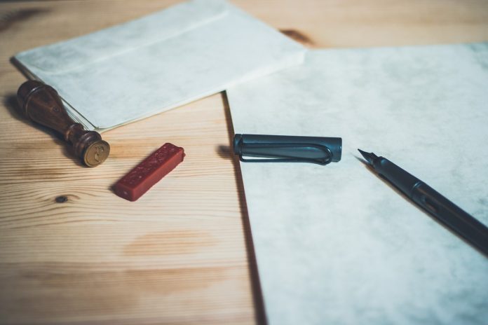 Fountain pen and stamp sitting on a brown surface with a piece of parchment and an envelope.