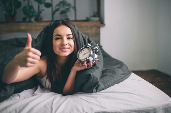 Pretty, happy girl waking up in the morning and switching off the alarm clock.