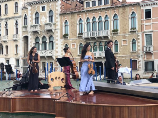 Closeup of a quartet of musicians standing on a giant violin, called 'Noah's Violin,' in the Grand Canal of Venice.