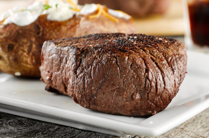 Closeup photo of a grilled steak with baked potato in background for dinner.