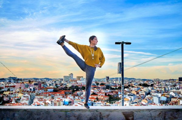 Young woman doing yoga exercise outdoors on the Lisbon city view background.