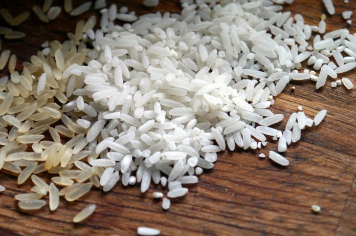 Grains of white rice sitting on a wooden surface.
