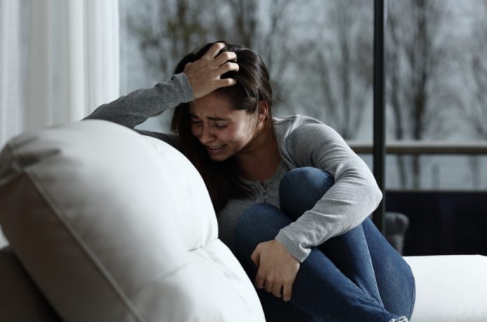 Young woman curled up on the couch and crying.