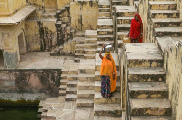 Indian women carrying jars to fill with water walk down into a stepwell.
