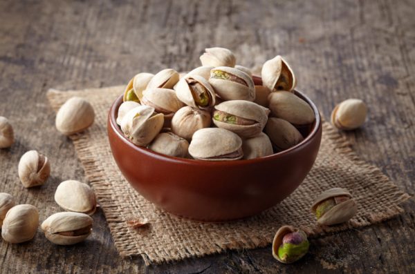 Pistachios in the shell in a bowl on a piece of burlap on a wooden surface.