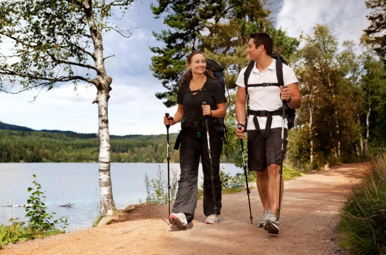 A couple walking on trail with backpacks using Nordic poles.