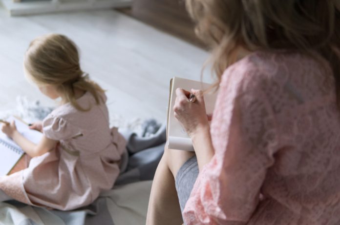 Mother sitting on the sofa and daughter sitting on the floor both writing lists.