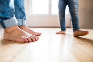 Closeup of a young father and daughter's bare feet standing on a hardwood floor.