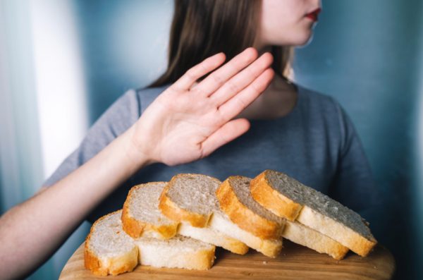 Young woman with head turned away and hand held up, refusing to eat sliced bread on a cutting board.