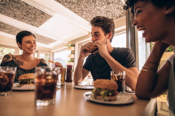 Friends talking and laughing together over a meal of burgers, fries, and sodas at a fast food restaurant.