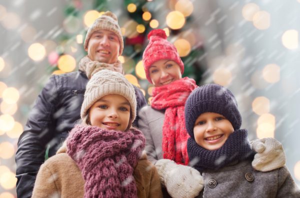 Happy family in winter clothes stand together outdoors in front of a decorated Christmas tree.