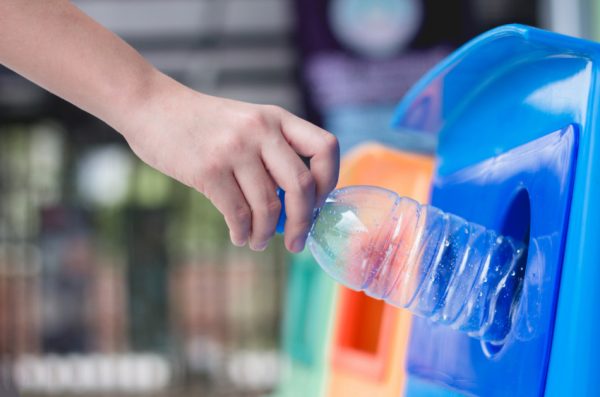 Woman throwing plastic bottle into recycle bin.