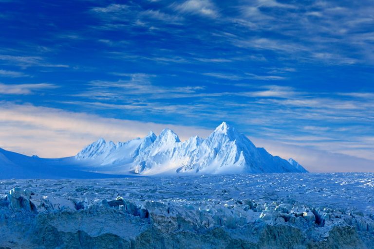 White snowy mountain, blue glacier, and ice in the ocean near Svalbard, Norway.