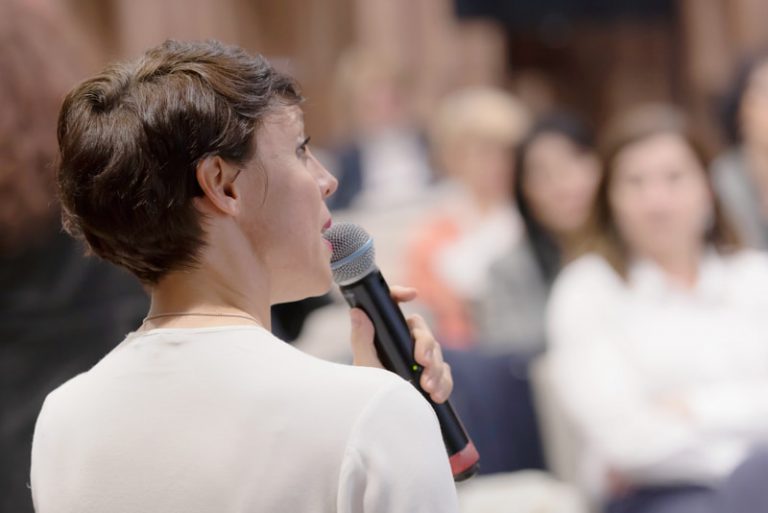 Woman holding a microphone to talk to an audience.