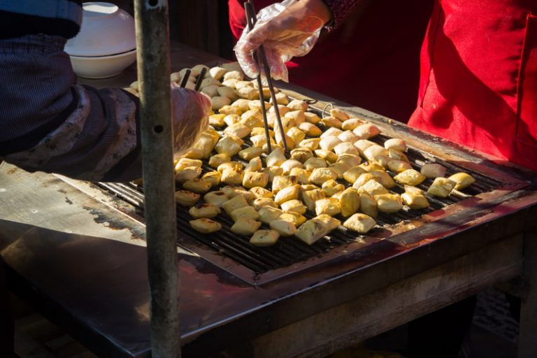 Blocks of stinky tofu being turned on a grill with chopsticks by two outdoor street vendors in China.