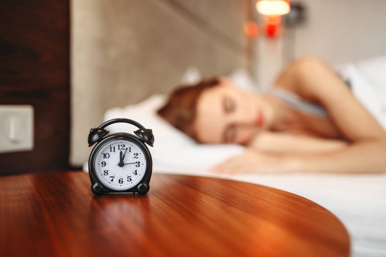 Woma laying in bed with a clock showing just after midnight.