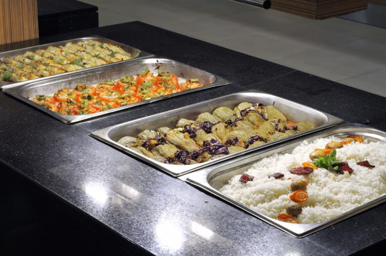 Four dishes at a self-service buffet in a luxury hotel including rice topped with meatballs and vegetables, fried dumplings, stuffed tomatoes, and artichoke hearts.