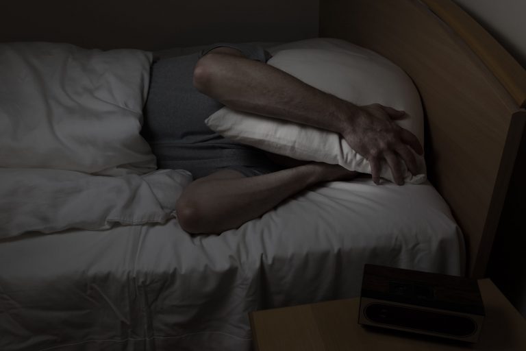 Man in bed with a pillow over his head.