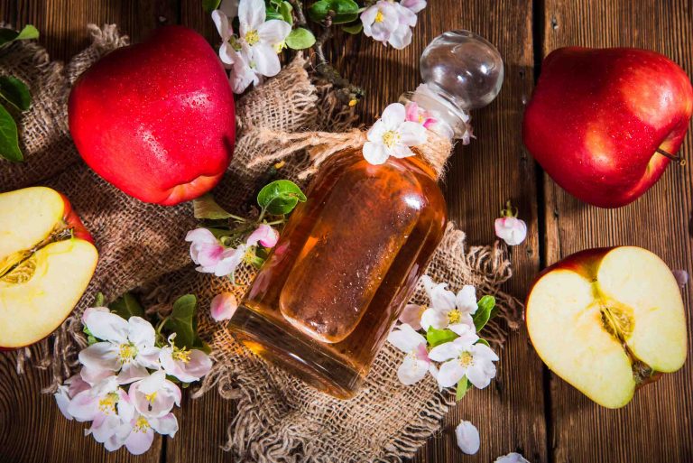 A bottle of vinegar and apples on a table with apple flowers.