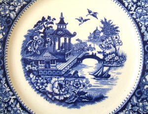 Porcelain plate with a decorative background showing details of the vintage blue and white willow pattern.
