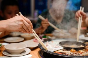 People taking food with chopsticks from a hot pot.