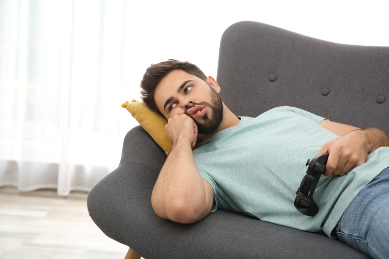 A bearded man laying on the couch holding a video game controller.