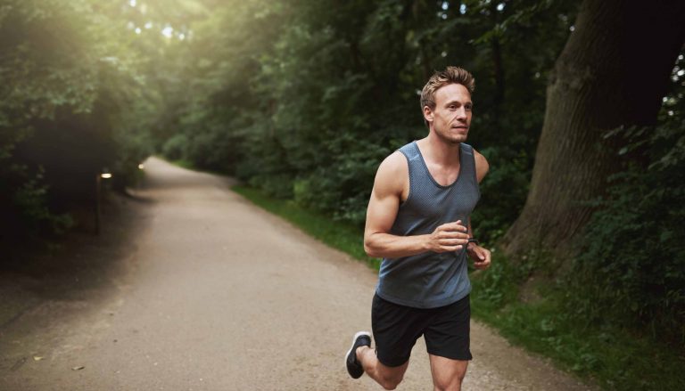 A man running for exercise down a forest park trail.