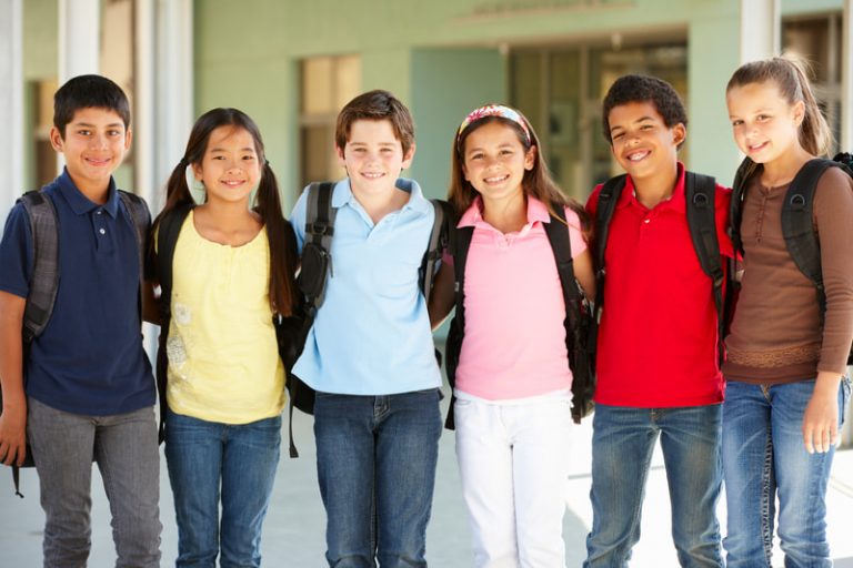 A group of pre-teen children wearing backpacks and posing together standing outside at school.