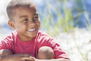 Smiling African American boy sitting on the beach.