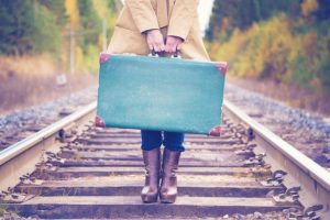 A woman standing on railraod tracks with a suitcase.